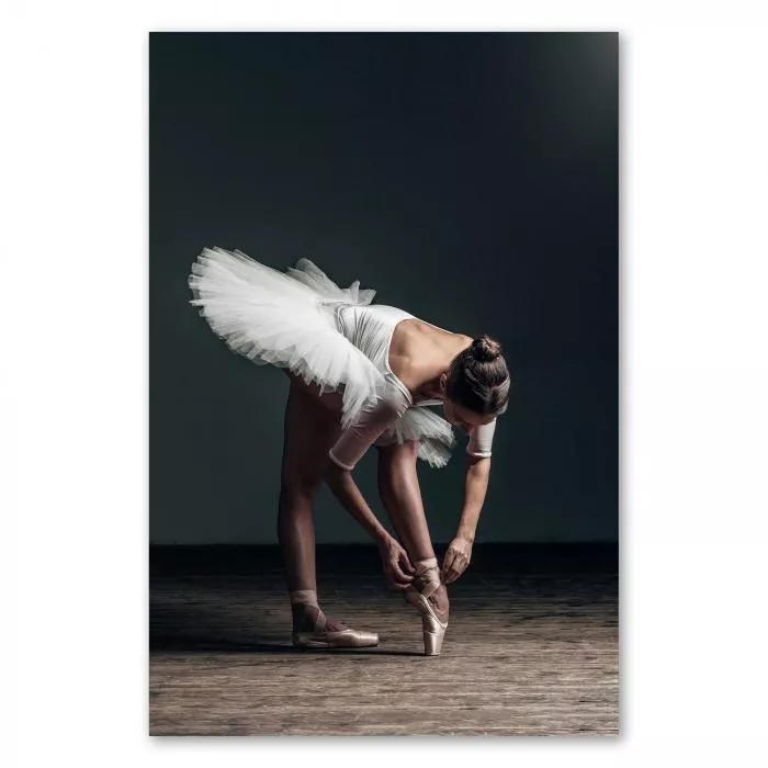 Eine grazile Ballerina in einem weißen Tutu bindet ihren Ballettschuh - ein Moment voller Anmut und Eleganz.