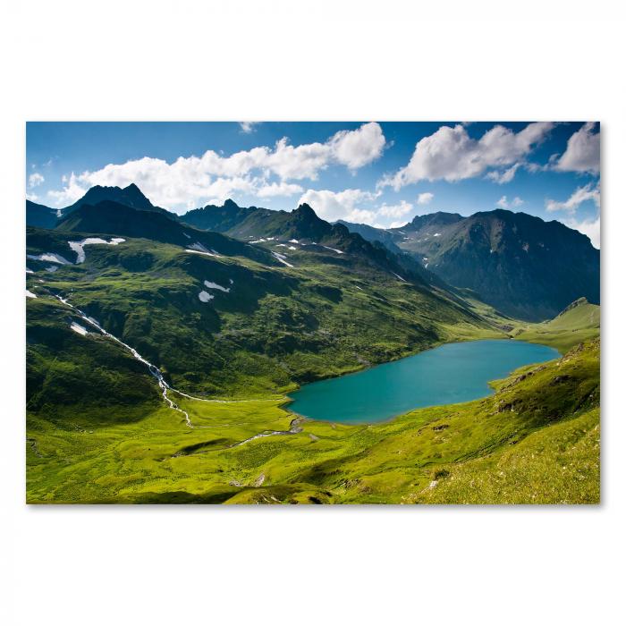 Kristallklarer, blauer Bergsee umgeben von grünen Hügeln und schneebedeckten Gipfeln, Wasserfall stürzt hinab.