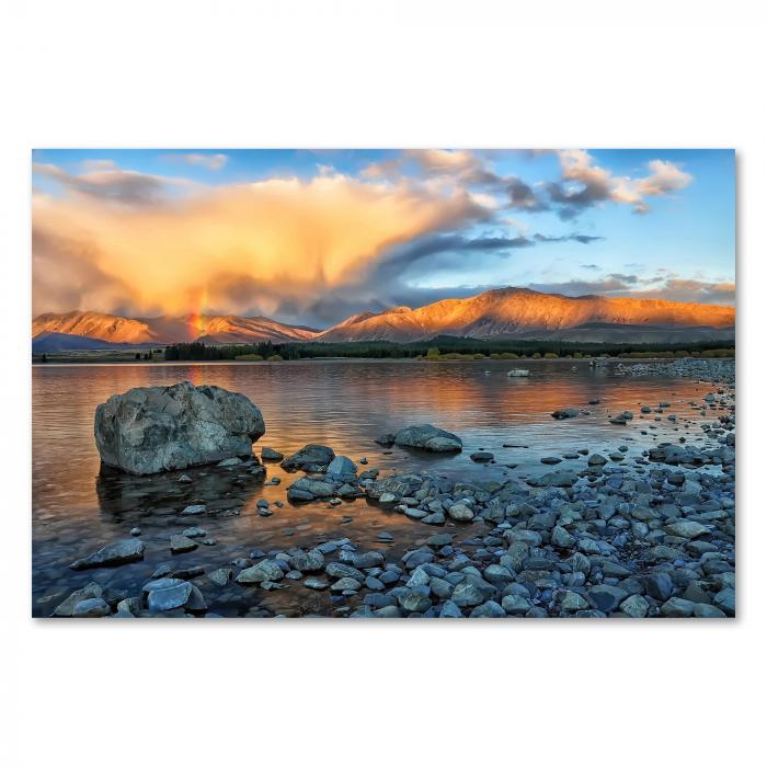 Strahlender Regenbogen über malerischem Bergsee, Sonne hinter Bergen, Wolken in warmen Farben.