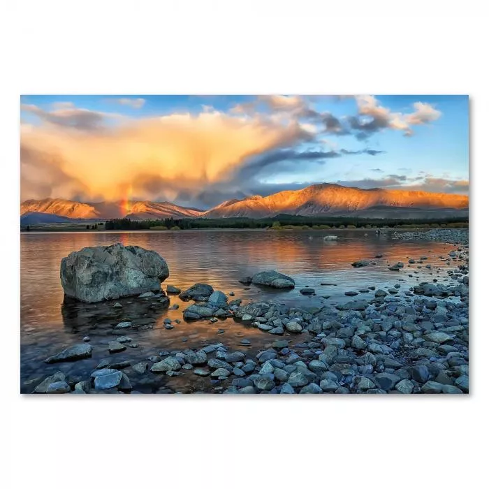 Strahlender Regenbogen über malerischem Bergsee, Sonne hinter Bergen, Wolken in warmen Farben.