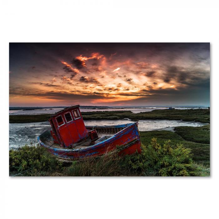 Ein verlassenes, rotes Boot liegt am Ufer, im Hintergrund ein farbenfroher Himmel.