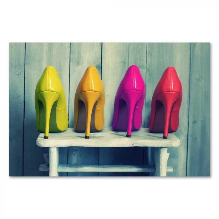 Vier bunte High Heels in Gelb, Orange, Pink und Rot stehen auf einer weißen Holzbank vor einer Vintage-Holzwand.