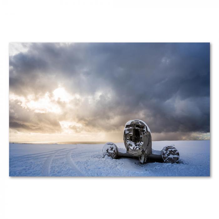 Ein verlassenes Flugzeugwrack liegt im Schnee, der Himmel ist von dramatischen Wolken und Sonnenstra hlen durchzogen.