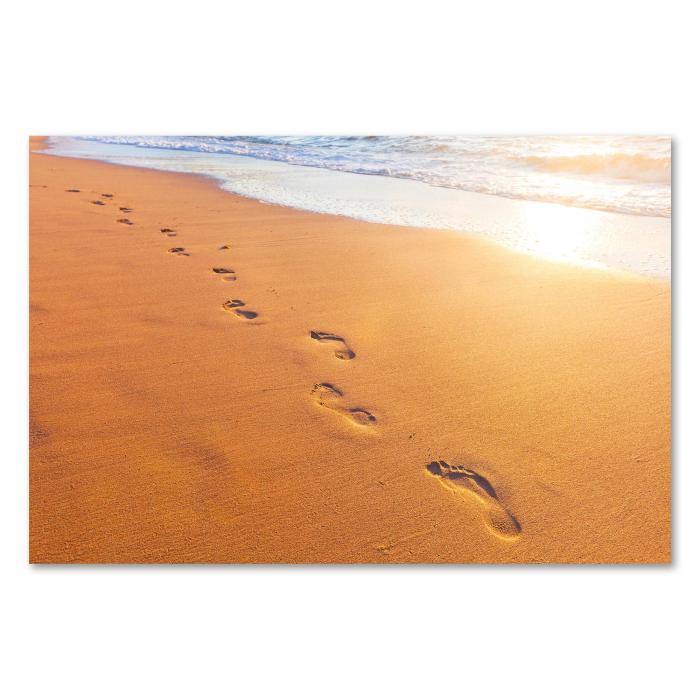 Fußabdrücke im Sand führen dem Horizont entgegen, wo die Sonne im Meer versinkt.