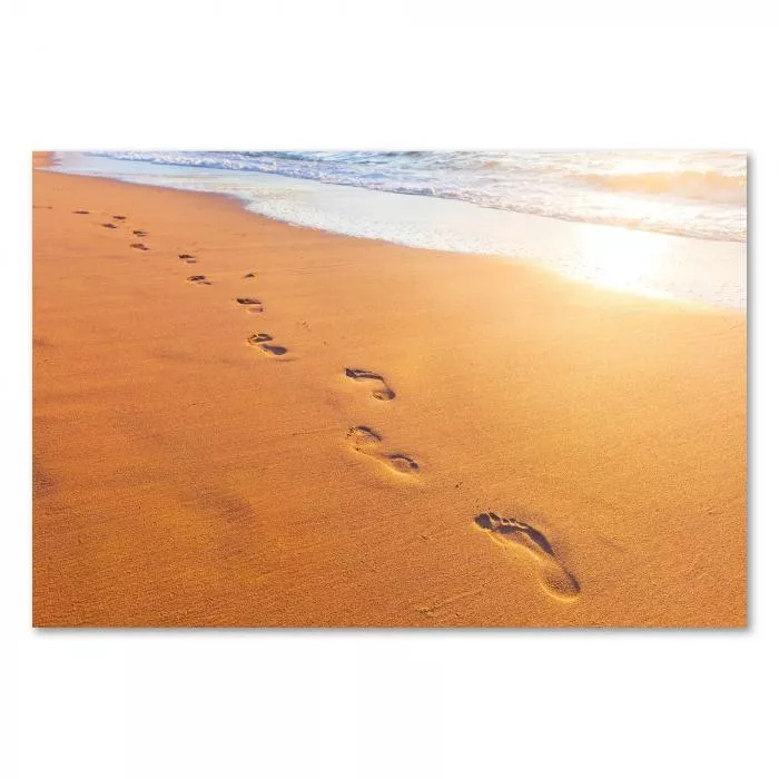 Fußabdrücke im Sand führen dem Horizont entgegen, wo die Sonne im Meer versinkt.