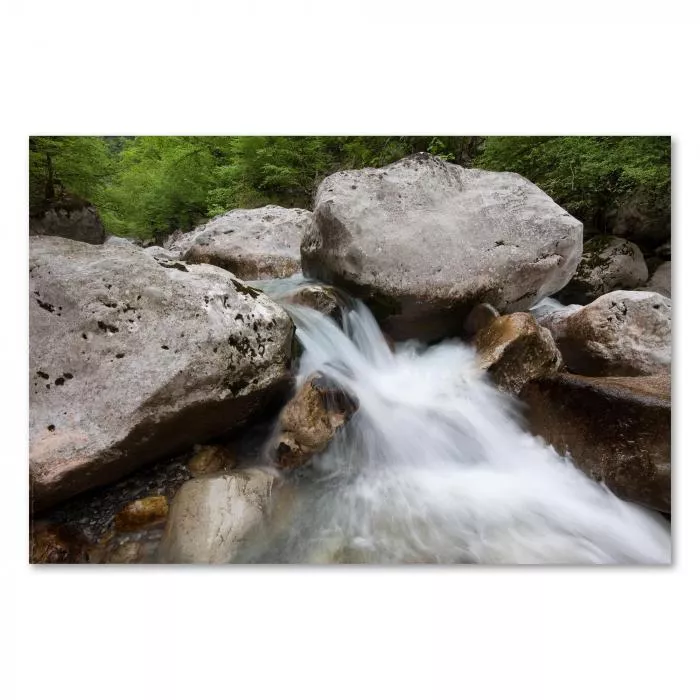 Gebirgsbach schlängelt sich durch felsige Landschaft, türkisfarbenes Wasser und grüne Bäume schaffen Idylle.