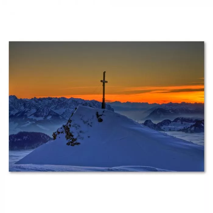 Ein Gipfelkreuz strahlt im Sonnenuntergang über einem atemberaubenden Alpenpanorama.