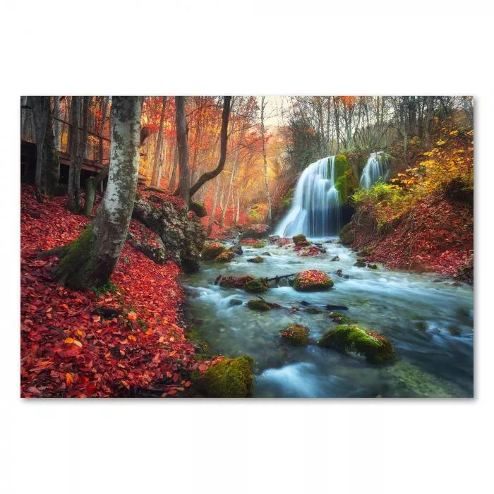 Wasserfall über bemooste Felsen, herbstlicher Wald, rote Blätter, magisches Licht.