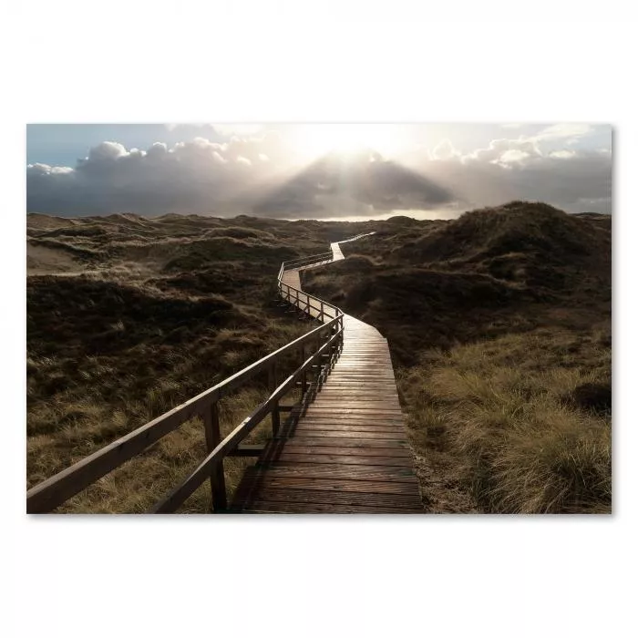 Ein Holzsteg schlängelt sich durch hohe Dünen, Sonnenstrahlen fallen durch die Wolken.