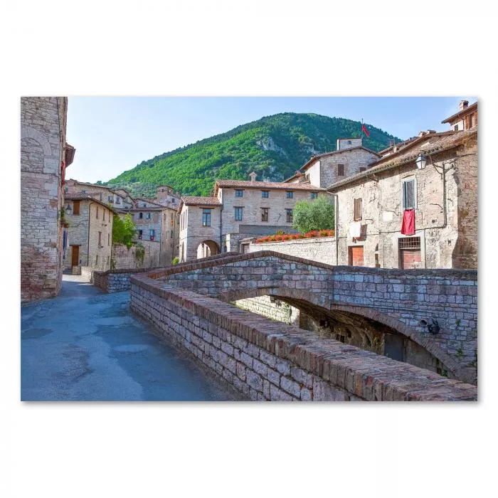 Weg durch Bergdorf, Steinbrücke über Bach, Häuser mit Fahnen am Hang - Italien.