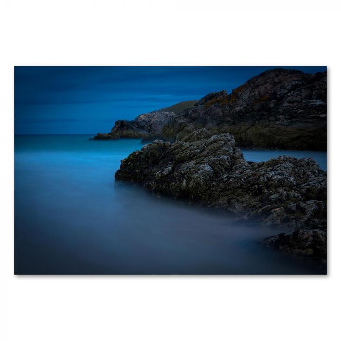 Mystische Abendstimmung an der Küste, Felsen ragen aus Wasser, Wellen rollen sanft an den Strand.