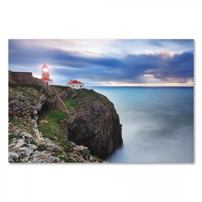 Leuchtturm auf einer Klippe am Meer, während Wellen gegen die Felsen schlagen.