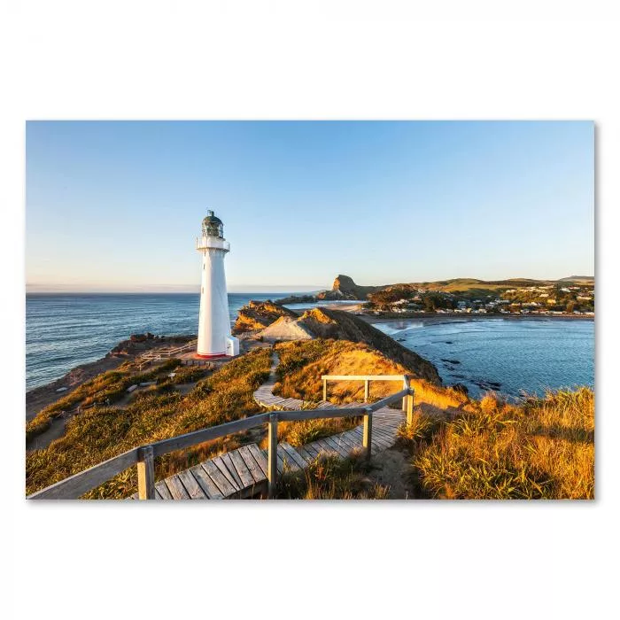 Ein weißer Leuchtturm auf einer Klippe wird von der aufgehenden Sonne in warmes Licht getaucht. Ein Holzsteg führt zum Leuchtfeuer und bietet einen atemberaubenden Blick.