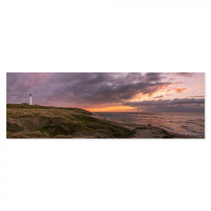 Ein Leuchtturm an der Küste bei dramatischem Sonnenuntergang - ein maritimes Panoramabild.