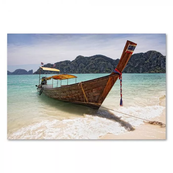 Ein traditionelles thailändisches Longtailboot liegt am Strand vor der Kulisse von grünen Inseln und blauem Himmel.