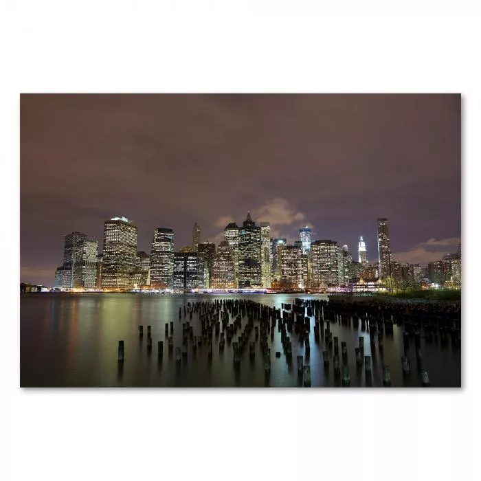 Skyline von Manhattan bei Nacht, im Vordergrund East River mit Holzpfählen.