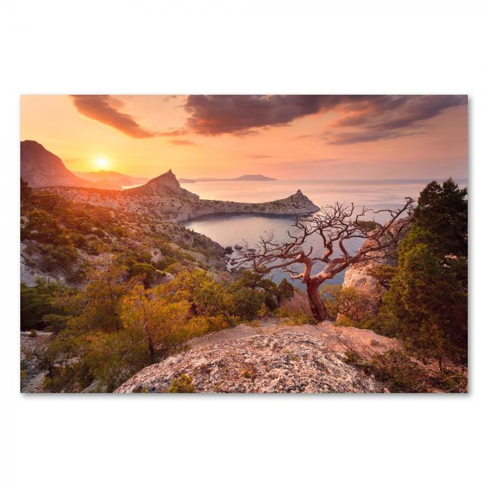 Von einem hohen Felsen aus hat man einen weiten Blick über die Küste. Die Sonne geht hinter den Bergen auf und taucht das Meer in goldenes Licht.