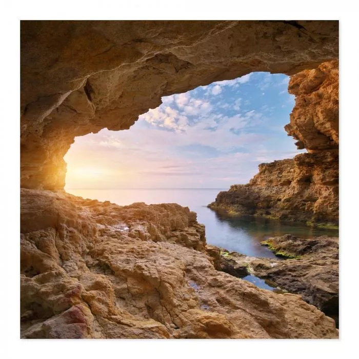 Blick aus Höhle auf Meer, Sonnenaufgang, warme Farben spiegeln sich im Wasser.