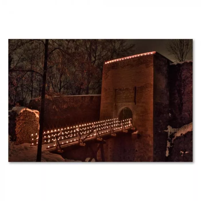 Eine mittelalterliche Burg mit beleuchteter Brücke in einer Winterlandschaft, die Szene wirkt magisch.