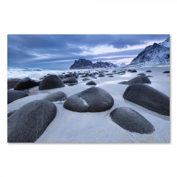 Schroffe Felsen, weißer Sandstrand, majestätische Berge, dramatischer Himmel.