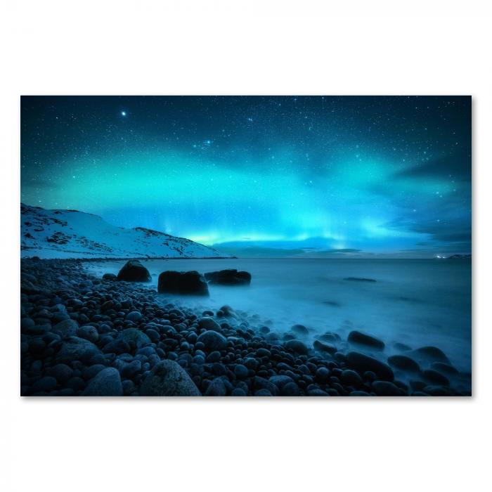 Leuchtend grüne und blaue Nordlichter tanzen am Himmel über einem felsigen Strand. Die Sterne funkeln hell und das Meer leuchtet im Schein der Aurora Borealis.