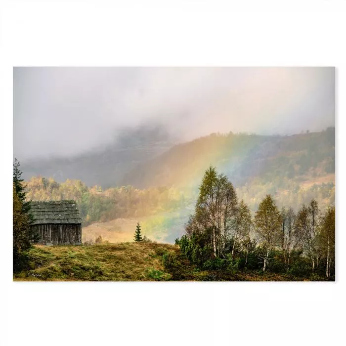 Ein bunter Regenbogen erstrahlt über einer Holzhütte in den Bergen, während Nebel die Landschaft bedeckt.