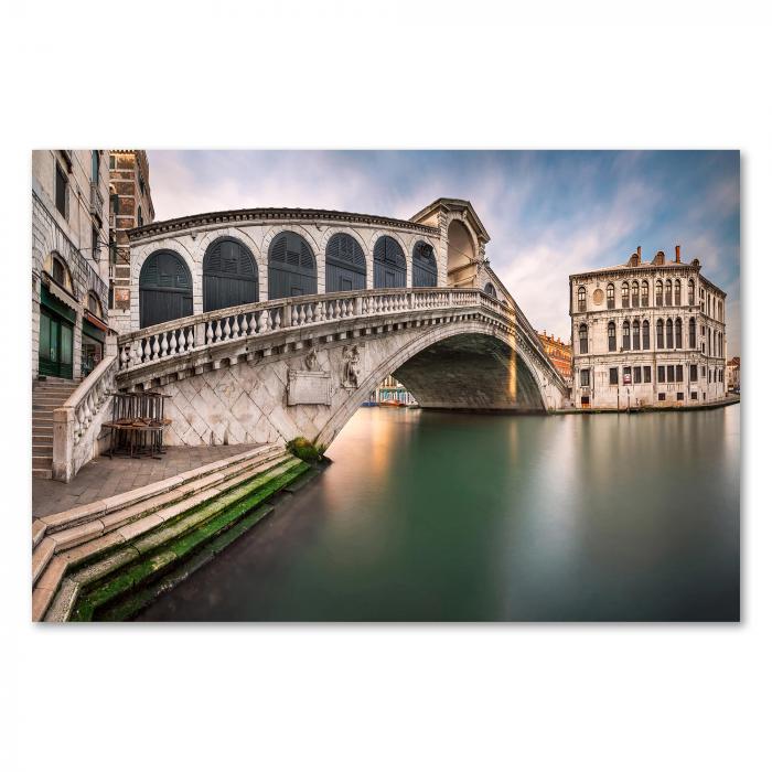 Rialtobrücke in Venedig, Sonnenaufgang, warme Farben spiegeln sich im Kanal.