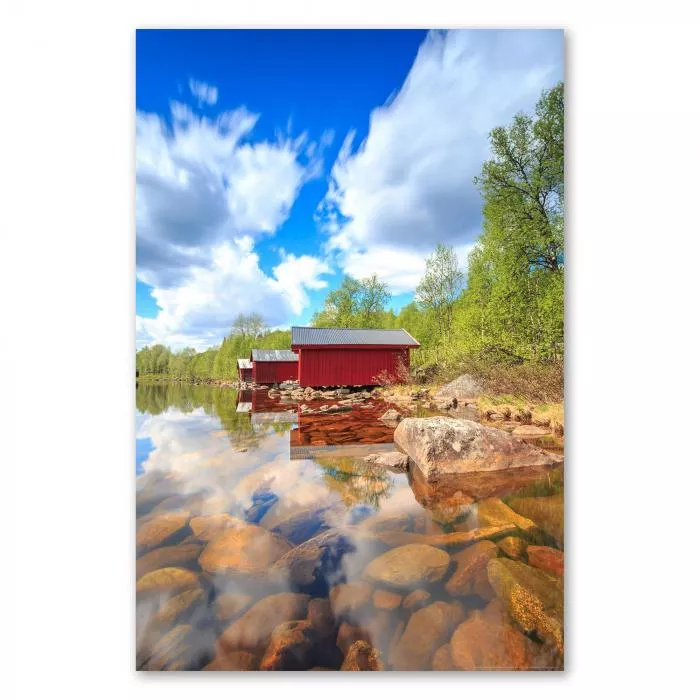 Drei rote Holzhütten am Ufer eines ruhigen Sees in Schweden.Die Wolken spiegeln sich im Wasser.