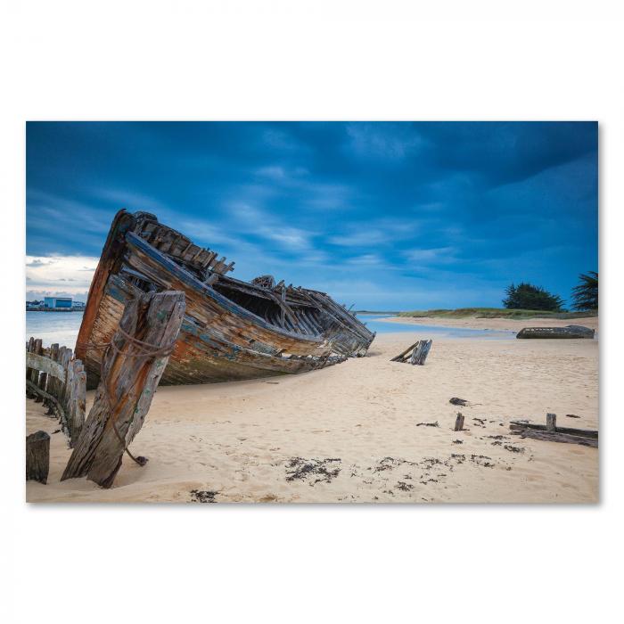 Verwittertes Schiffswrack am Sandstrand, blauer Himmel, dramatische Wolken.