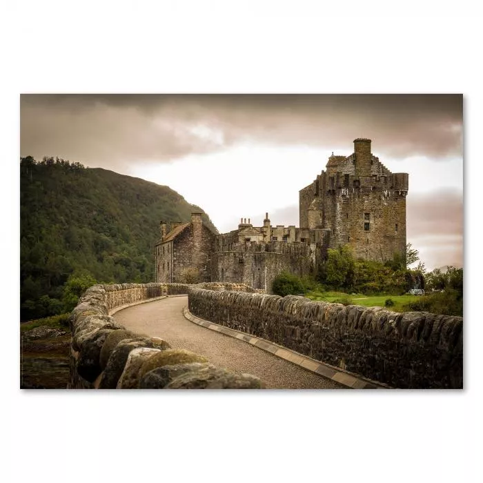 Gepflasterte Straße führt zu imposantem Schloss in Schottland, grüne Hügel schaffen mystische Atmosphäre.