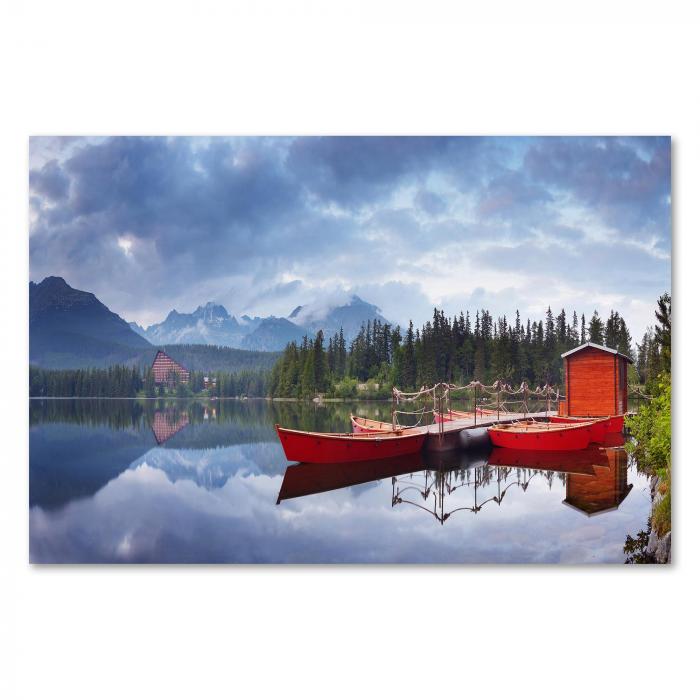 Ruhiger See, grüne Wälder, Berge spiegeln sich im Wasser, rote Boote am Ufer.