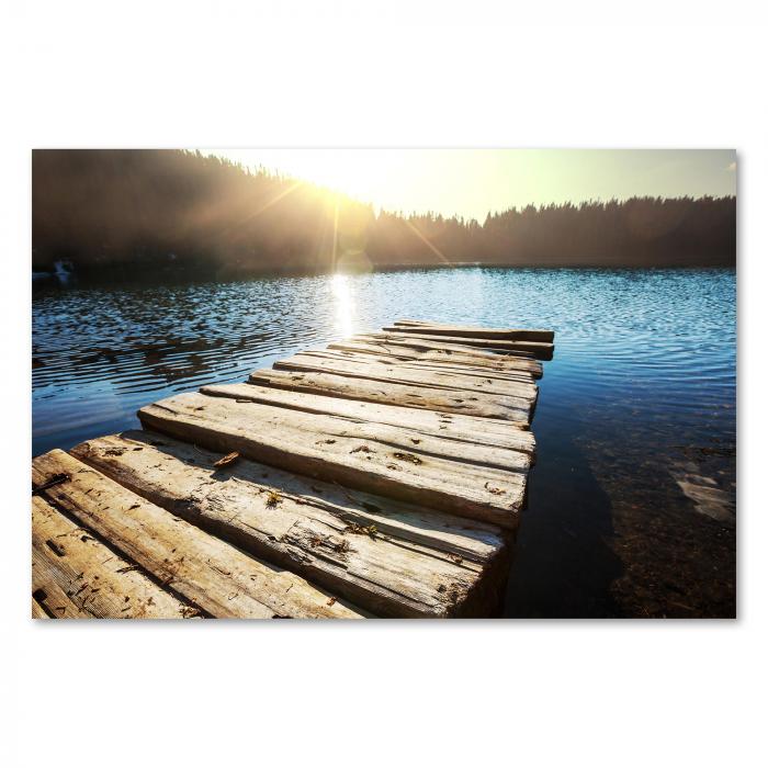 Ein Steg führt auf einen idyllischen Bergsee, die Sonne versinkt hinter den Hügeln – ein Moment der Ruhe und Schönheit.