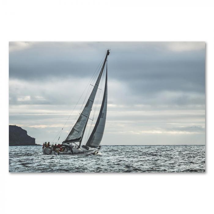 Ein Segelboot kämpft sich durch die hohen Wellen einer stürmischen See. Die grauen Wolken und das aufgewühlte Wasser vermitteln die Kraft der Natur und die Herausforderungen der Seefahrt.