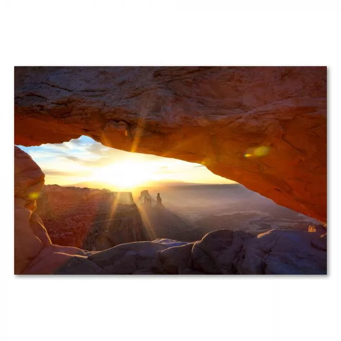 Die aufgehende Sonne taucht einen weiten Canyon in goldenes Licht, Blick durch einen natürlichen Felsbogen.