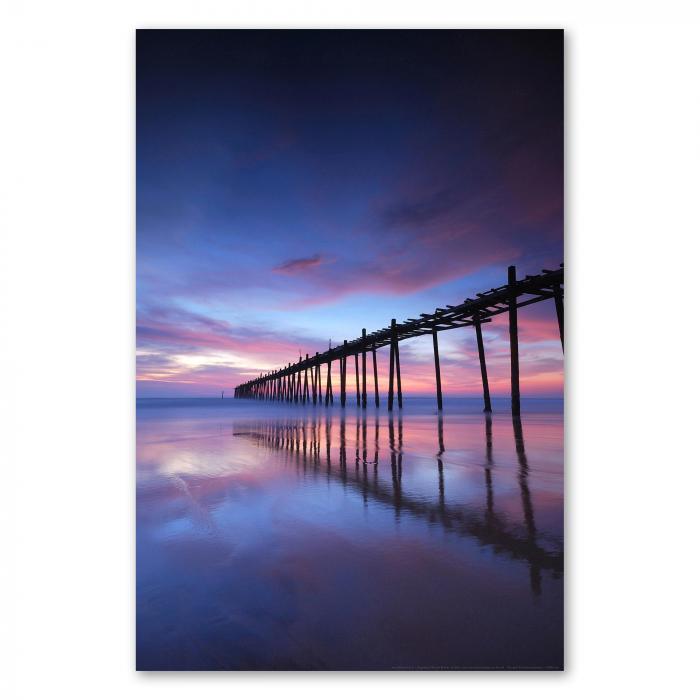 Holzsteg ragt ins Meer, atemberaubender Sonnenuntergang in Rosa- und Lilatönen spiegelt sich im Wasser.