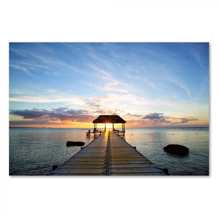 Ein Holzsteg führt zu einem Pavillon im Meer, die Sonne geht unter – ein traumhaftes Bild von Urlaub und Entspannung.