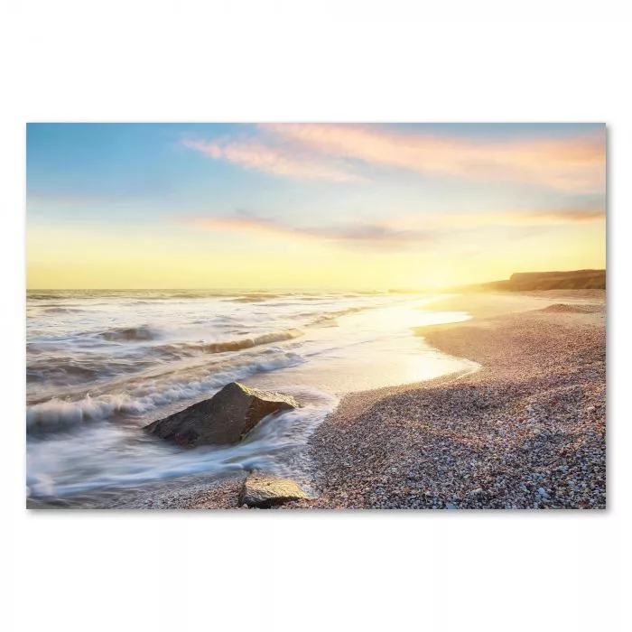 Sonnenuntergang am Strand, warmes Licht, Wellen, einzelner Felsen im Meer.