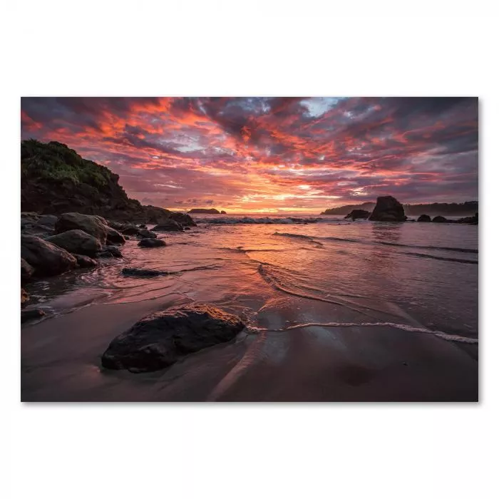 Atemberaubender Sonnenuntergang in Rottönen taucht einen Strand mit Felsen und Wellen in warmes Licht.