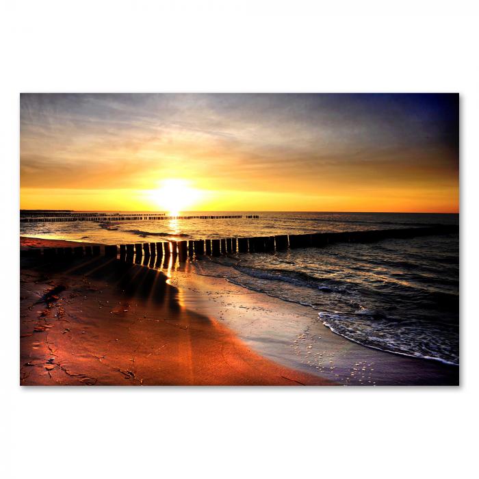 Sonnenuntergang am Strand, warmes Licht, Holzpfähle, lange Schatten.