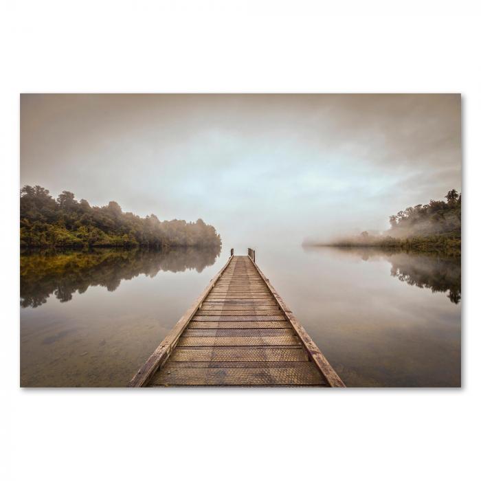 Ein Holzsteg führt über einen nebligen See. Die Spiegelung des Wassers und die diffuse Lichtstimmung erzeugen eine ruhige, fast mystische Atmosphäre.