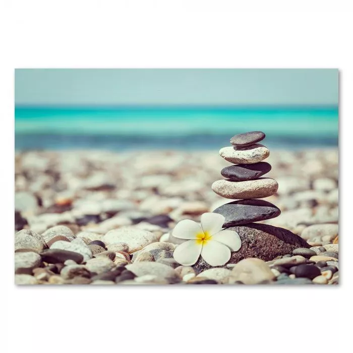 Ein Turm aus Steinen steht am Strand, türkisblaues Wasser & eine weiße Blume.