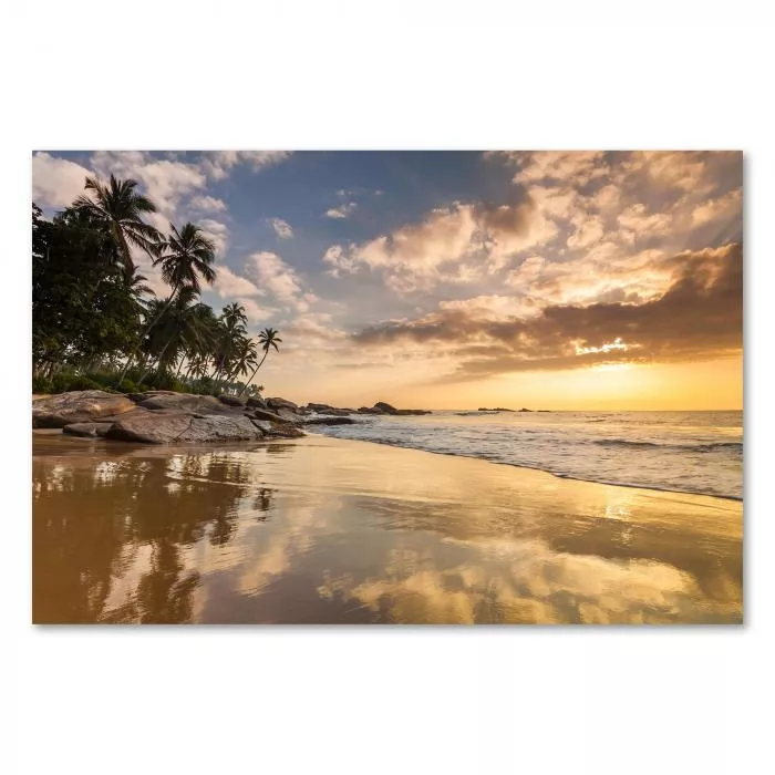 Goldenes Sonnenuntergangslicht taucht Sandstrand mit Palmen & Felsen in warme Farben.