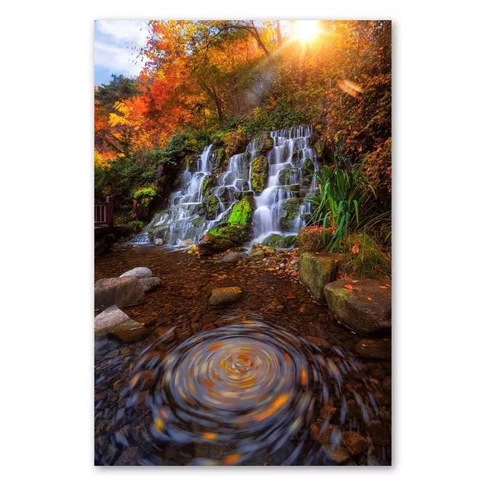 Wasserfall, moosbewachsene Felsen, herbstliche Blätter, Sonnenlicht.