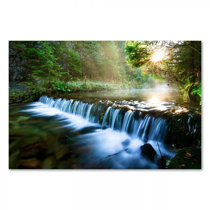 Sonnenstrahlen erhellen einen kleinen Wasserfall im Wald - ein idyllisches Bild voller Ruhe.