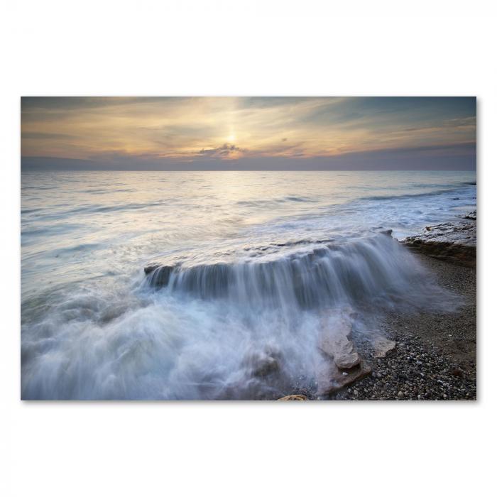 Sanfte Wellen treffen auf das felsige Ufer des Toten Meeres. Die untergehende Sonne taucht die Szenerie in warmes Licht und erzeugt lange, dramatische Schatten.