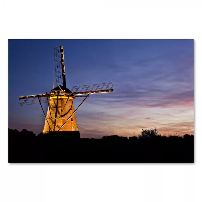 Eine beleuchtete Windmühle steht silhouettiert vor dem Abendhimmel mit orange-violetten Wolken.