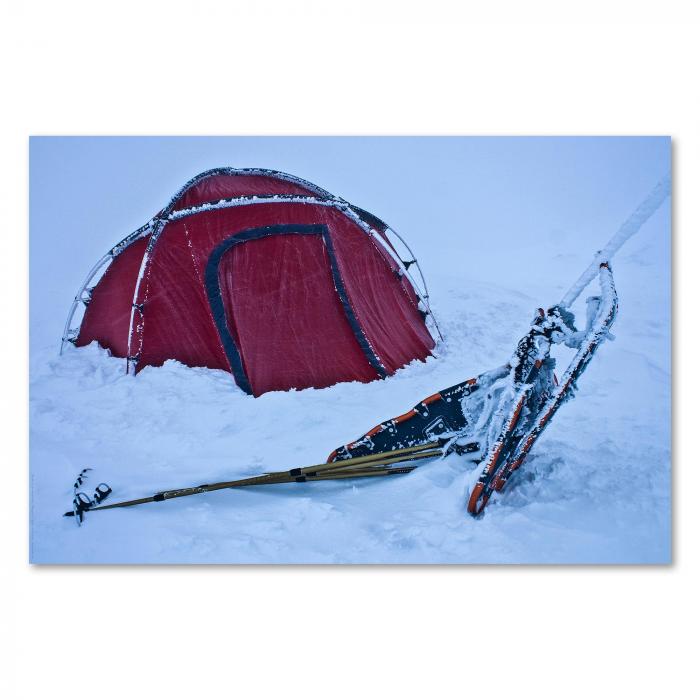 Rotes Zelt in schneebedeckter Landschaft, daneben Schneeschuhe und Wanderstöcke bereit zum Abenteuer.