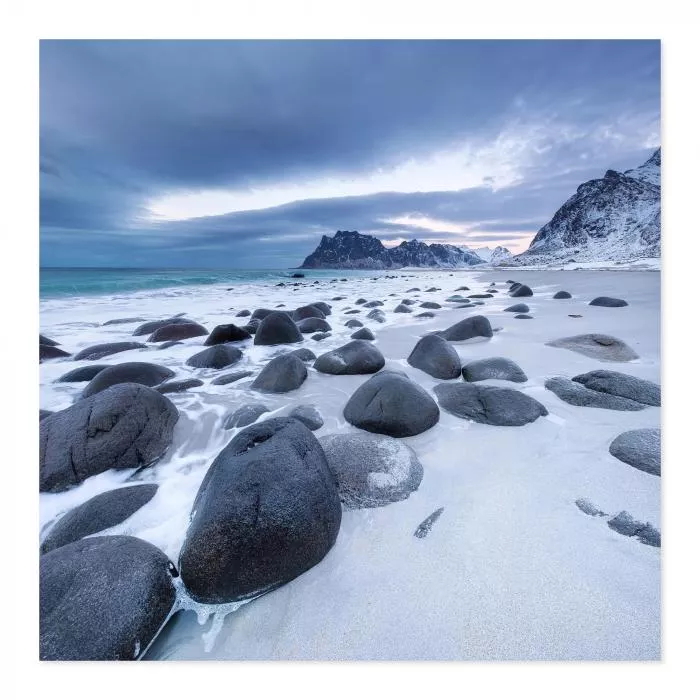 Strand, schwarze Steine, Schnee, Wellen, Berge im Hintergrund - dramatisch.