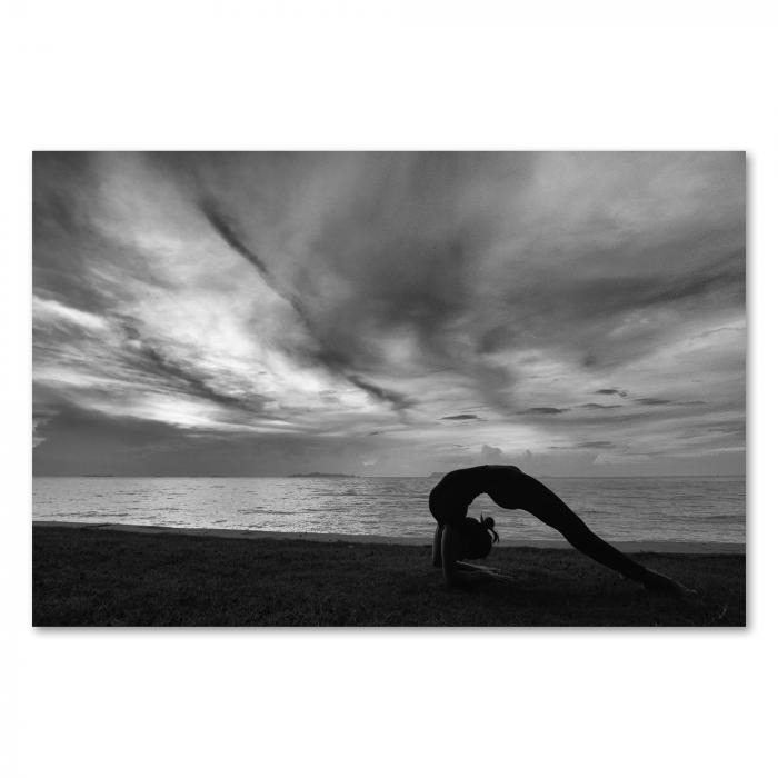 Schwarz-Weiß-Foto: Frau in Yoga-Kleidung, Brücke-Pose, Strand, Meer, bewölkter Himmel.