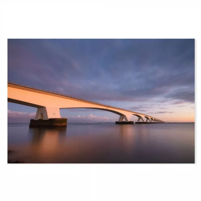 Zeelandbrücke bei Sonnenuntergang, Spiegelung im Wasser, orangefarbener Himmel.